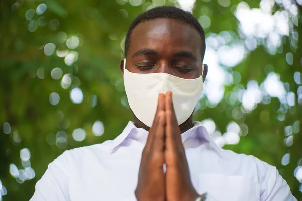 Afrikalı adam virüs koruması için beyaz gömlek ve yüz maskesi takıyor. Yazılı. Dünya koronası virüsü covid-19 için yeşil arka plan üzerine dua et.