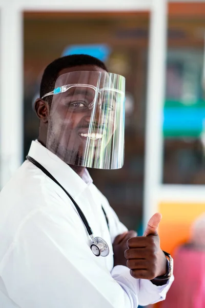 African doctor wear face shield and holding stethoscope with kind and smiling