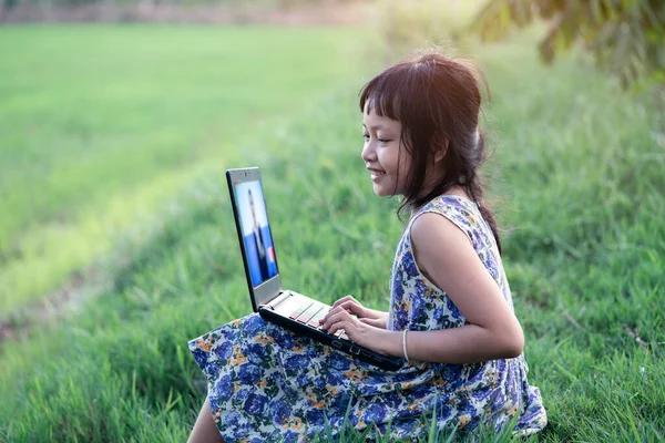 Happy children learning outdoor by studying online and working on laptop in green field