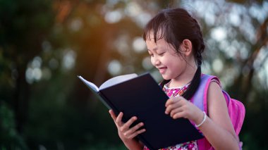 Sırt çantasıyla kitap okuyan küçük liseli kız. Okul konseptine geri dön.