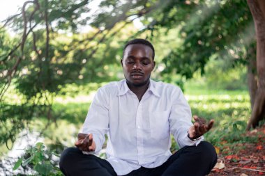 Afrikalı adam yeşil doğa parkında oturuyor ve meditasyon yapıyor..