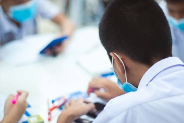 Asyalı üniformalı öğrenciler sınıfta ders çalışmak için maske takıyorlar..