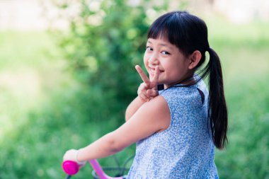 Asyalı küçük kız dışarıda bisikletini sürüyor. Gülümsüyor ve mutlu.