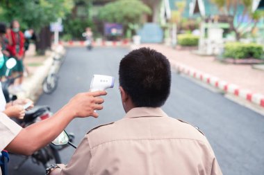 Öğretmen, okulda virüs kovid-19 semptomlarını korumak için öğrenciyi kontrol etmek için kızılötesi termometre tabancası kullanıyordu.