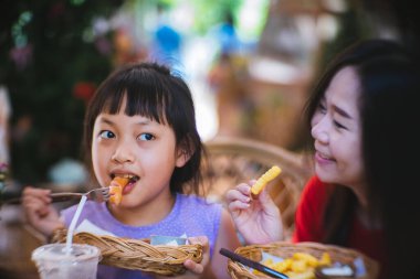 Asyalı anne ve kızı mutlulukla sosis yiyorlar.