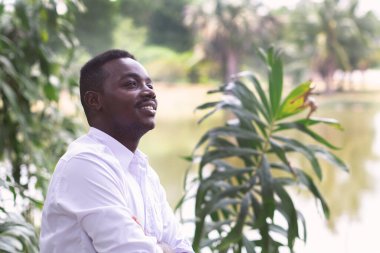 Beyaz gömlekli Afrikalı iş adamı yeşil doğayla ilgileniyor ve düşünüyor.