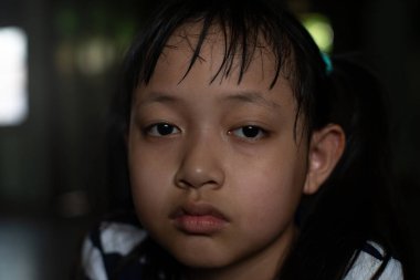 Asyalı küçük kız yalnız ve üzgün bir şekilde yukarı bakıyor ve düşünüyor.