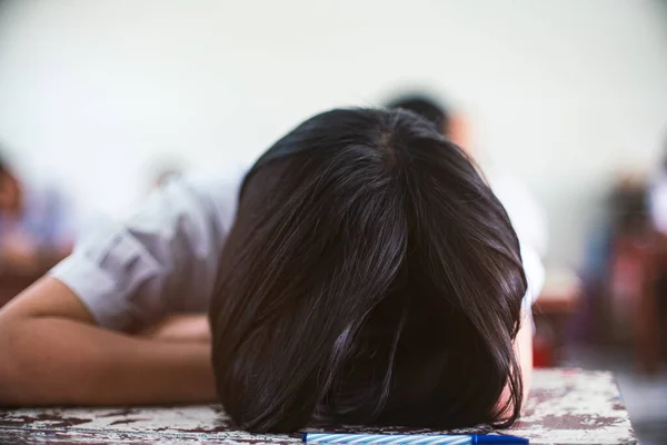 Tired uniform student sleeping in a exam test classroom