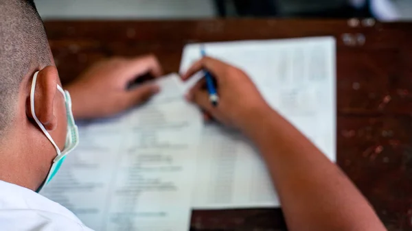 Corona virüsünü veya Coperid-19 'u korumak için maske takan ve stres altında okulda sınav kağıtları hazırlayan öğrenci.