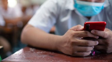 Üniformalı öğrenciler akıllı telefon kullanarak ve sınıfta koruyucu yüz maskesi takarak çevrimiçi veya test sınavı çalışmaktadırlar.