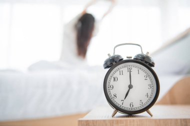 Çalar saat kapanıyor. Arka planda mutlu bir kadın var. Uyandıktan sonra yatakta uzanıyor..