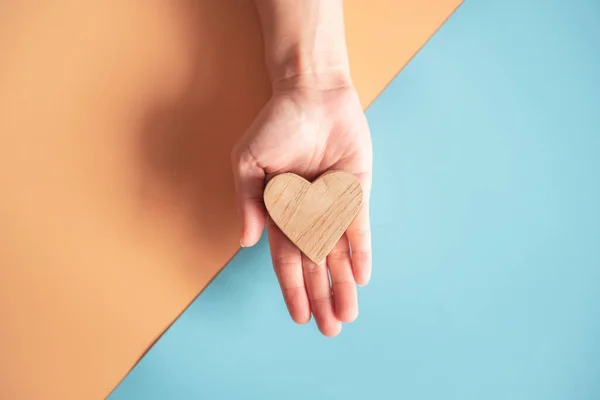 Manos Sosteniendo Corazón Madera Sobre Fondo Papel Color Azul Naranja —  Fotos de Stock