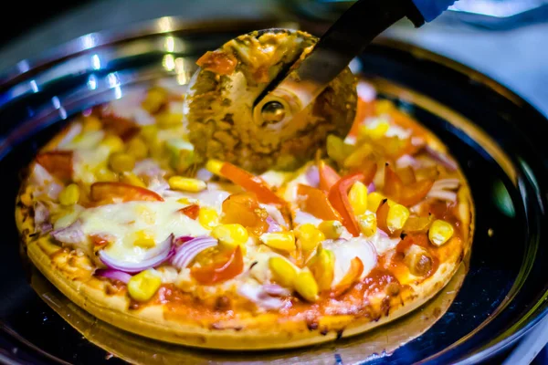 Cutting cheese pizza with Pizza cutter, with tomato, onion, corn toppings, with selective focus in lockdown.