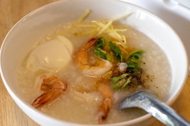 Haşlanmış pirinç çorbası ve ahşap masada beyaz kâsede karides.