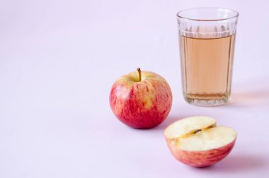 Bir bardak elma suyu ve pembe arka planda tam bir buçuk kırmızı elma.