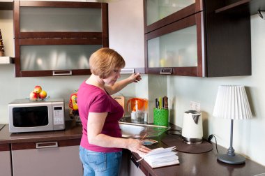 Mutfakta yemek tarifi okuyan bir kadın.