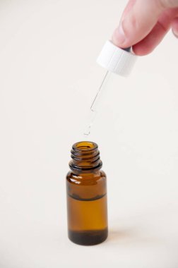 Siyah bir cam şişenin üzerinde pipeti tutan el, burun damlası, göz damlası