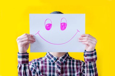 Sarı arka planda ekose gömlekli bir kız elinde beyaz bir kağıt tutarak neşe içinde gülümsüyor