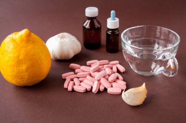 Tıbbi hayat: tabletler, bir kupa su, limon, sarımsak ve ilaç kahverengi arka planda şişelerde