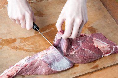 Kadın eli, tahta bir arka planda bıçakla çiğ et kesti.