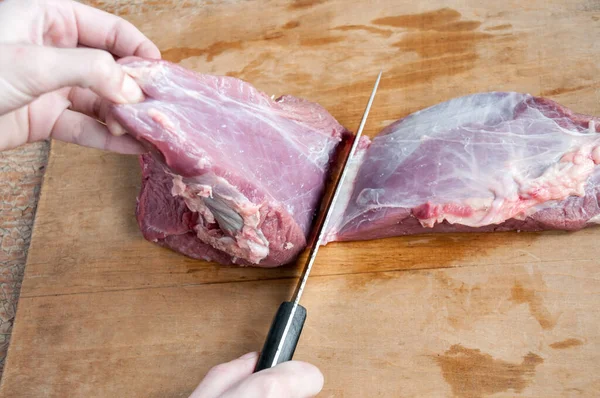 Women\'s hands cut a piece of raw beef meat with a knife on a wooden background