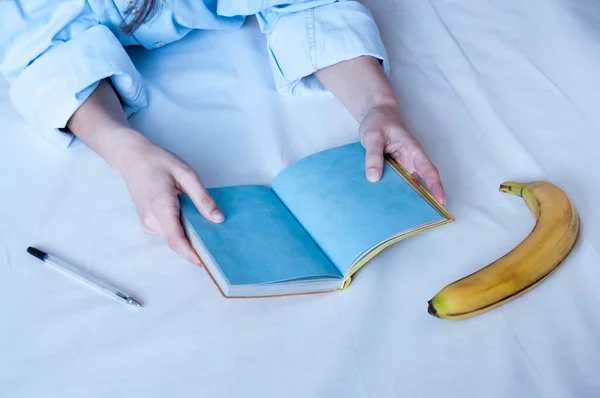Девушка Держит Пустую Синюю Тетрадь Лежит Постели Лежит Рядом Бананом — стоковое фото