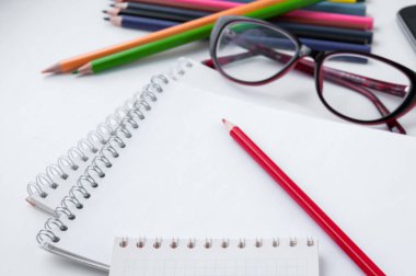 Beyaz bir not defterinde kırmızı kalem, birkaç tane de kalem ve gözlük.