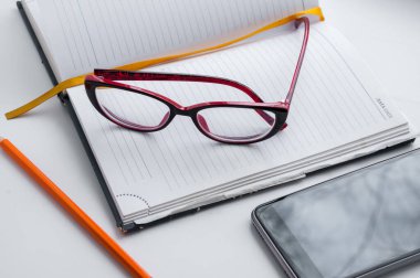 Günlük, gözlük, turuncu bir kalem ve akıllı telefon.