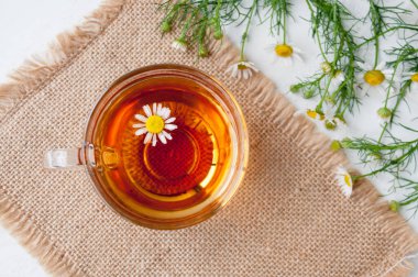 Masanın üstünde bir fincan papatya çayı ve papatya çiçeği.