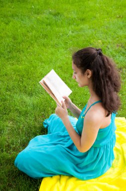 Esmer, çimlerin üzerinde bir kitapla oturuyor.