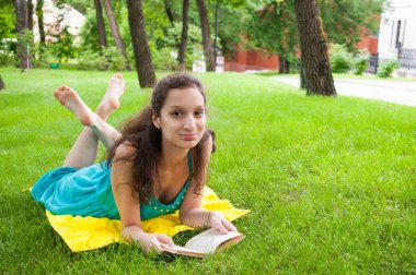 Esmer kız bahçede kitap okuyarak dinleniyor.