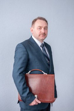 Takım elbiseli bir işadamı kahverengi evrak çantasıyla duruyor.