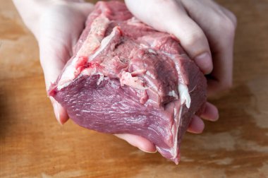 Kadın eli, tahta bir arka planda çiğ et parçası tutuyor.