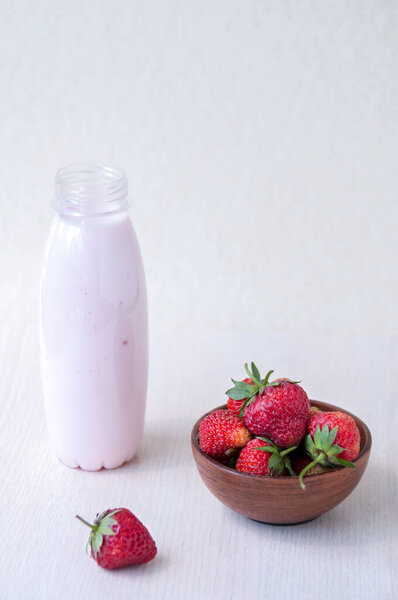 Red strawberries in a clay Cup and yogurt in a bottle on the table, summer Breakfast