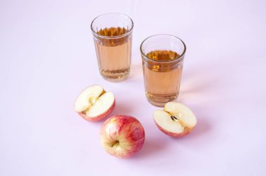 Kırmızı elma suyu ve pembe arka planda iki bardak elma suyu.