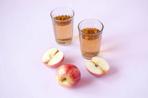 Whole and cut red Apple and two glasses of Apple juice on a pink background