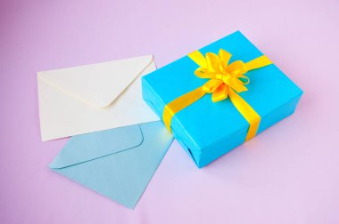 Mavi bir kutuda, sarı bir fiyonk ve pembe bir arka planda zarflar.