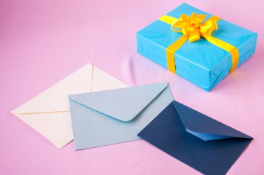 Mavi bir kutuda, sarı bir fiyonk ve pembe bir arka planda zarflar.