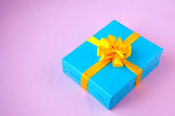 Gift in a blue box with an yellow bow on a pink background