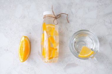 Bir bardak su, bir dilim portakal ve bir şişe narenciye, masanın üstünde.