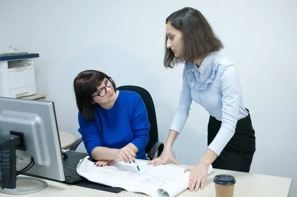 Office, a woman in a blue dress and a brunette girl working with drawings at a Desk