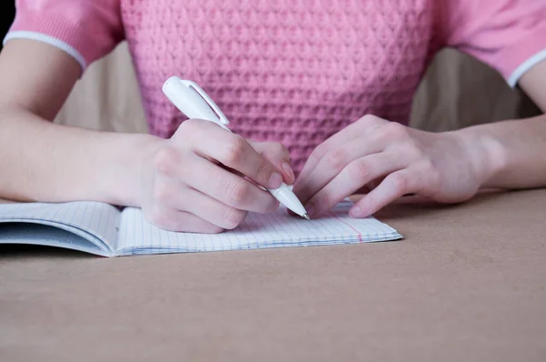 一个穿着粉色衬衫的女孩用钢笔在笔记本上写字 — 图库照片