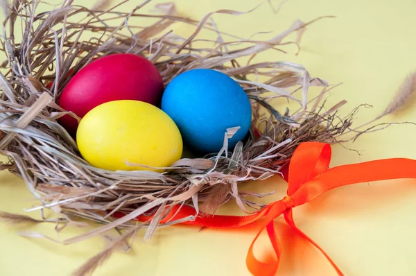 Easter colorful eggs in a nest with an orange ribbon on a yellow background