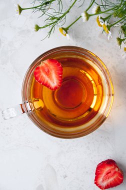 Bir fincan çilek çayı, çilek çileği masadaki papatya çiçekleri, üst manzara.