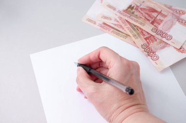 Bir kadının eli, beyaz bir kağıda kalemle, büyük Rus banknotlarıyla, borçların makbuzları kavramını yazar.