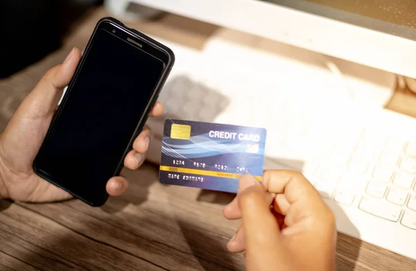 Hand holding credit card and mobile phone, The credit card prepare for customer and entrepreneur using for online shopping, e-commerse, business and internet banking with laptop.