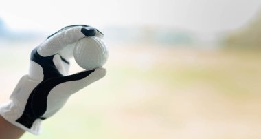 Beyaz profesyonel eldivenler giymiş, sol eli golf topunu tutan bir kadın golf sahasında golf topuna vurmaya hazırlanıyor.