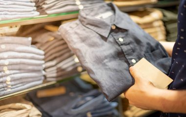 Erkek el, mağazadaki kumaş mağazasındaki askıda işaretli pamuk polo tişört için kıyafet seçiyor. Giyim ürünlerinin fiyatını, indirimini ve tanıtımını kontrol et.