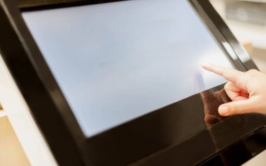 Kamu alanının önündeki tablet bilgisayara dokunan kadın eli, ürünün bilgilerini veya tanımını bulanık arkaplan sahibi müşteriye ulaştırmak için.