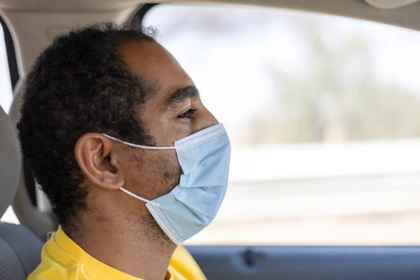 An Arabic man in the United Arab Emirates driving between Al Ain and Abu Dhabi wearing a protective face mask